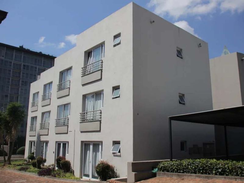 Exterior view of a modern multi-story apartment building featuring private balconies with metal railings and a covered parking area.