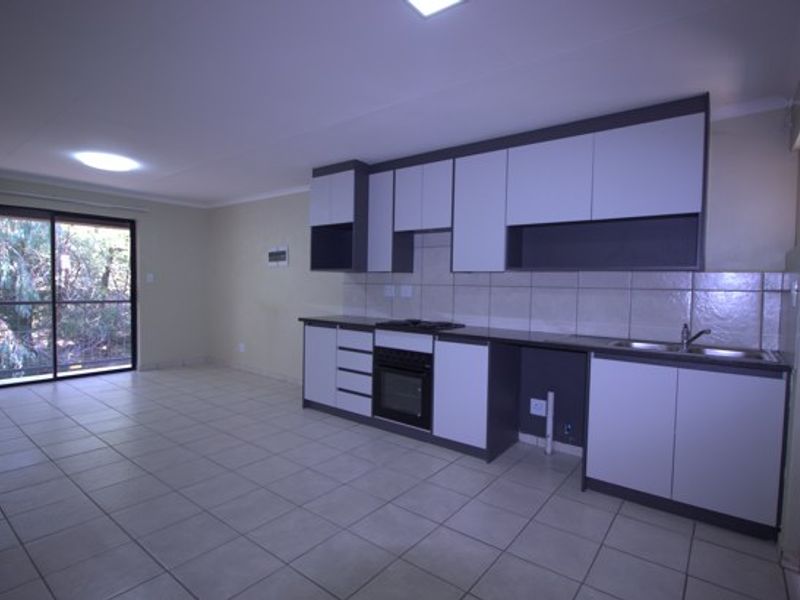 An open-plan living and kitchen area featuring modern two-tone cabinetry, built-in oven, tiled flooring, and a sliding door leading to an outdoor space.