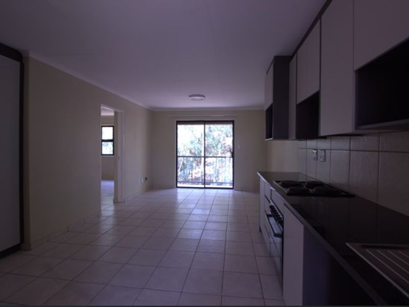 Open-plan living area featuring a functional kitchen with built-in cabinetry, oven, and hob, leading to a bright space with tiled flooring.
