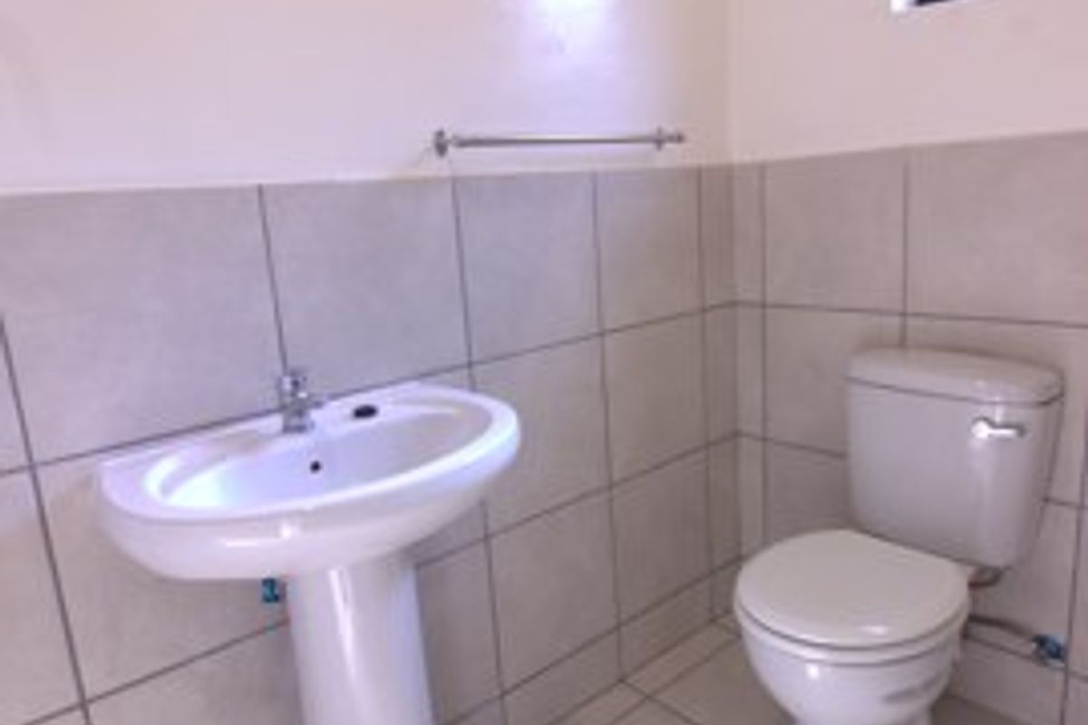 A clean, functional bathroom featuring a pedestal basin, ceramic toilet, and neutral wall and floor tiling.