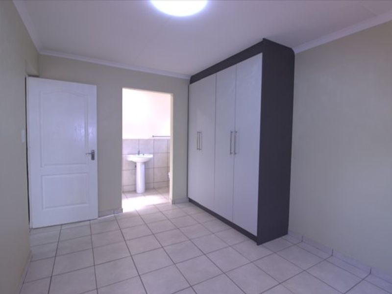A clean, empty bedroom featuring tiled flooring, built-in cupboards, and an en-suite bathroom with a pedestal basin.