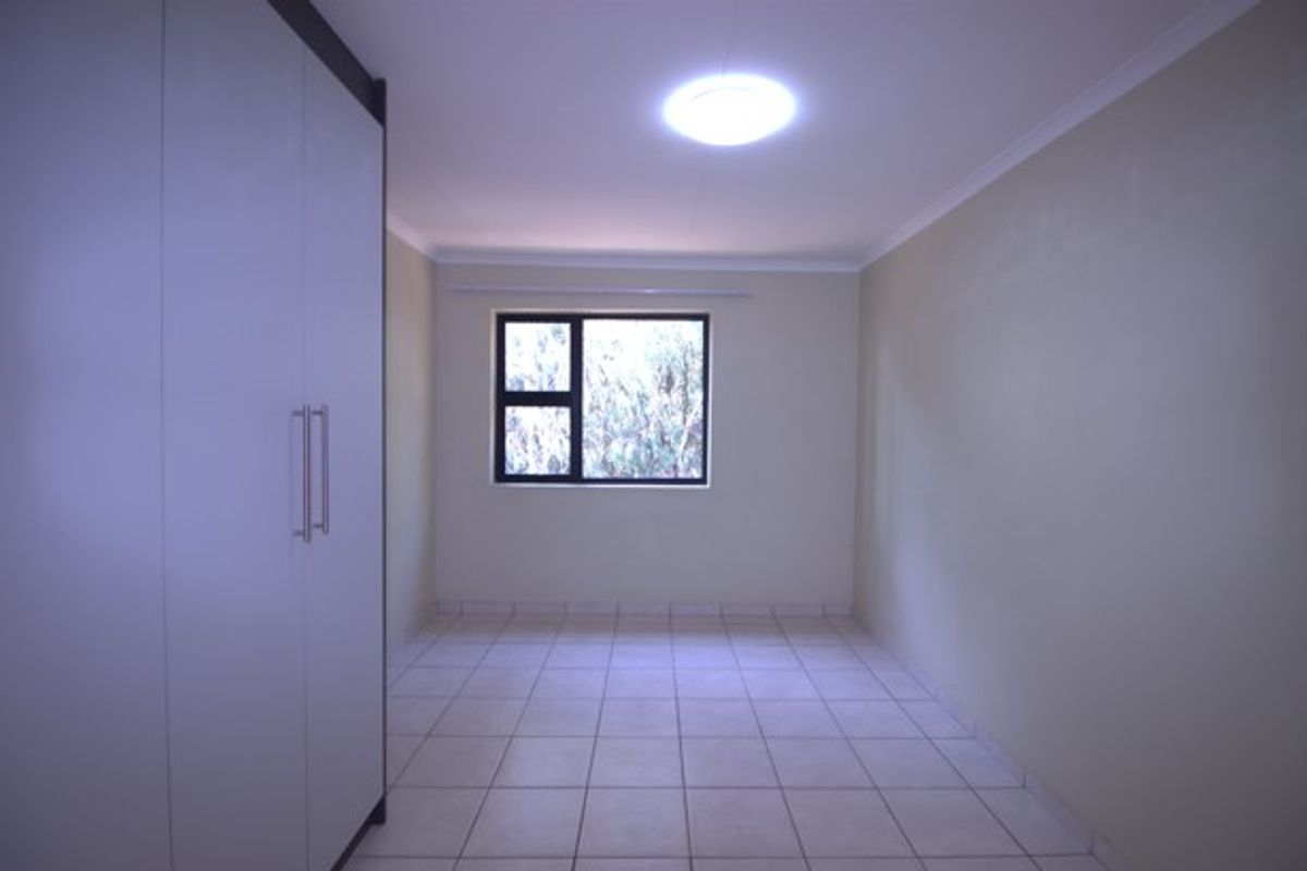 A clean, empty bedroom featuring neutral tiled flooring, built-in cupboards, and a window providing natural light.