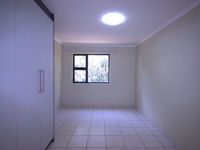 A clean, empty bedroom featuring neutral tiled flooring, built-in cupboards, and a window providing natural light.