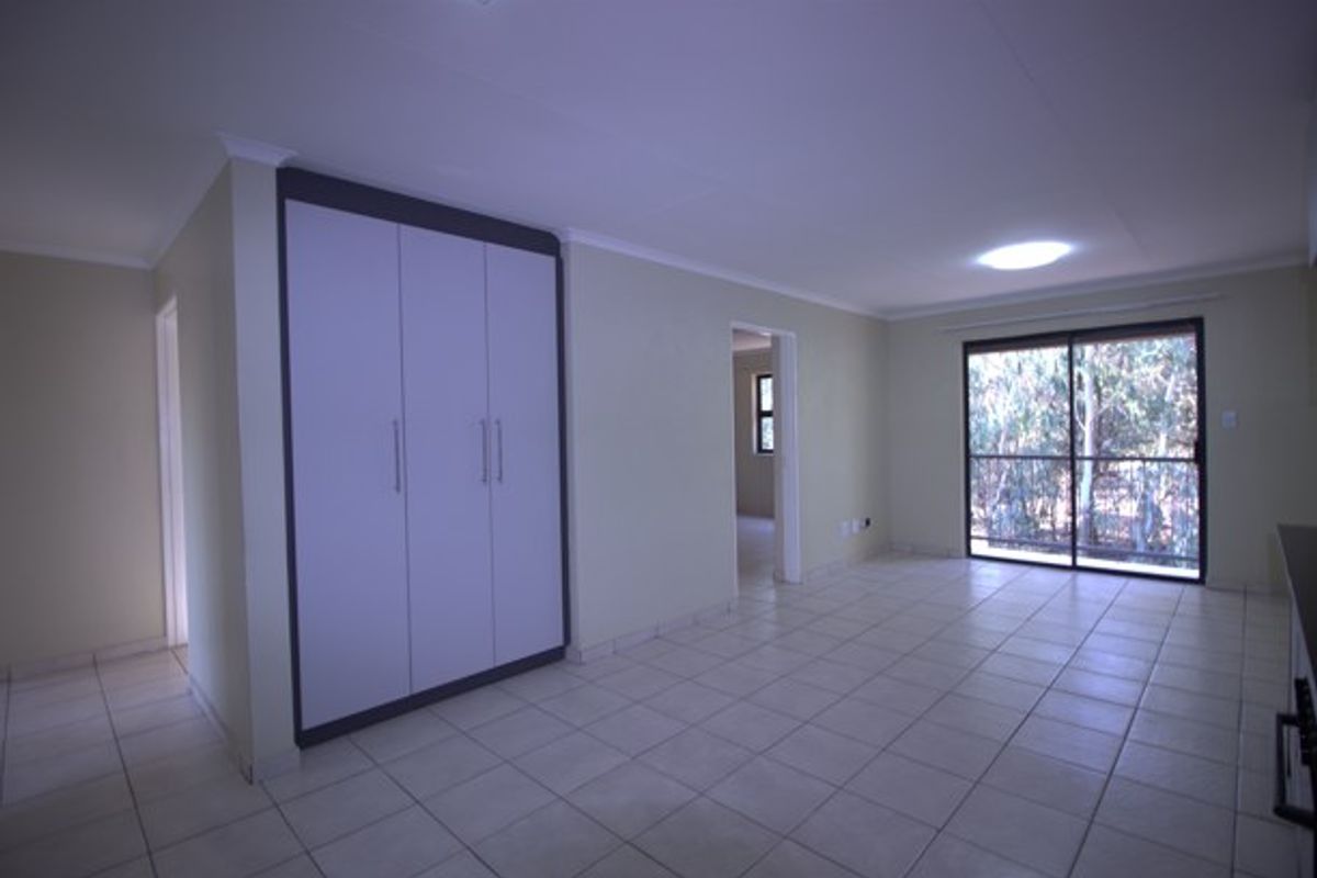 An open-plan living area featuring neutral tiled flooring, built-in storage cupboards, and a sliding glass door providing natural light and outdoor access.