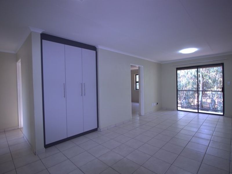 An open-plan living area featuring neutral tiled flooring, built-in storage cupboards, and a sliding glass door providing natural light and outdoor access.