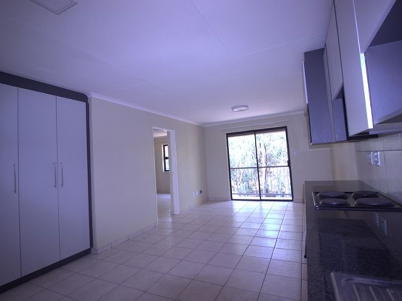 Spacious open-plan living area featuring a modern kitchen with built-in cabinetry, electric hob, granite countertops, and direct access to a balcony through sliding doors.