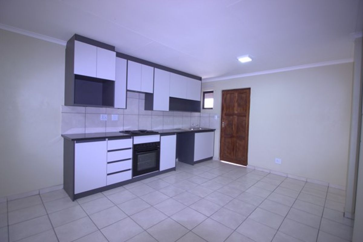 A clean, empty kitchen featuring modern two-tone cabinetry, built-in oven and hob, tiled splashback, and neutral floor tiles with direct access to an exterior door.