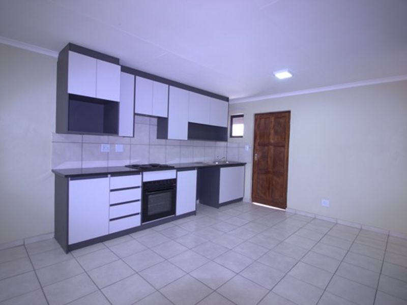 A clean, empty kitchen featuring modern two-tone cabinetry, built-in oven and hob, tiled splashback, and neutral floor tiles with direct access to an exterior door.