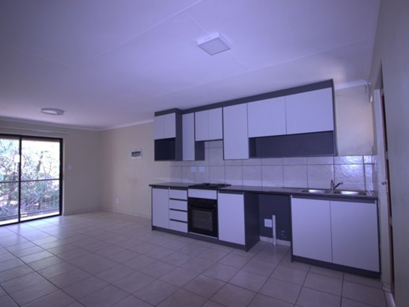 An open-plan living and kitchen area featuring tiled flooring, built-in cabinetry, a fitted oven and hob, and a sliding glass door leading outdoors.