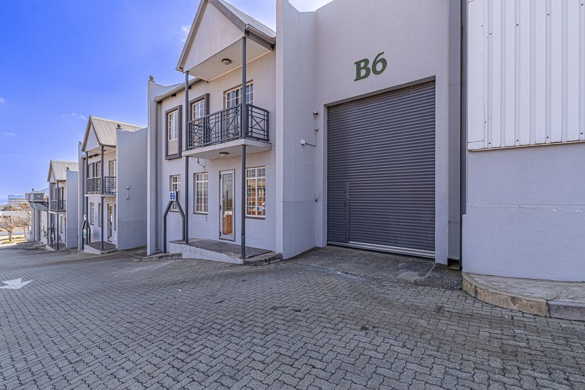Industrial unit featuring a large roller shutter door, paved driveway access, and a small balcony with metal railing.