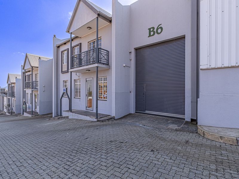 Industrial unit featuring a large roller shutter door, paved driveway access, and a small balcony with metal railing.