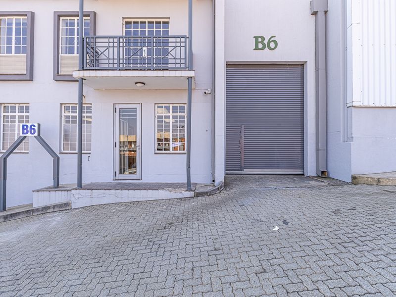 Industrial unit exterior featuring a roller shutter door, paved driveway access, and a small balcony above the entrance.