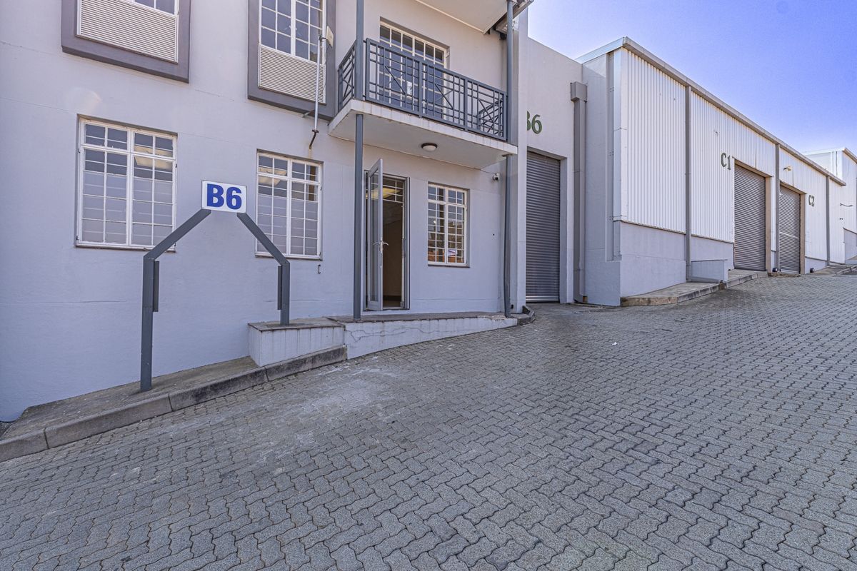 Industrial unit exterior featuring a paved driveway, roller shutter access, and a small balcony, providing functional access for commercial operations.