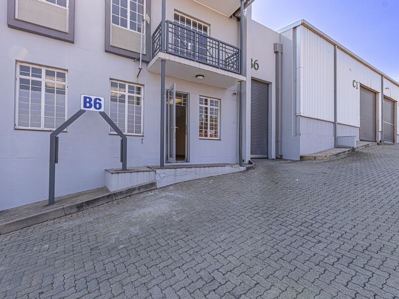 Industrial unit exterior featuring a paved driveway, roller shutter access, and a small balcony, providing functional access for commercial operations.