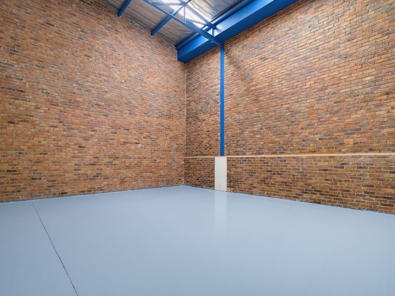 Spacious industrial utility area featuring high ceilings, exposed brick walls, blue steel structural beams, and a clean epoxy-coated concrete floor.