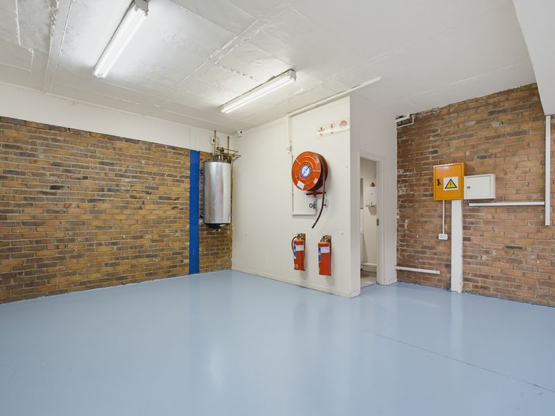 A clean, functional industrial utility space featuring exposed brick walls, durable epoxy flooring, and essential fire safety equipment including a hose reel and extinguishers.