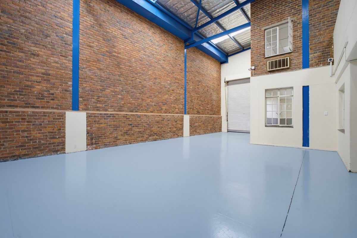 Spacious industrial utility area featuring exposed brick walls, high-clearance steel roof trusses, durable epoxy flooring, and a large roller shutter door for easy access.
