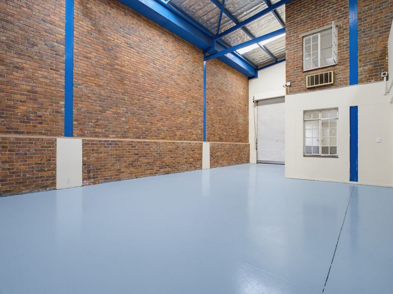 Spacious industrial utility area featuring exposed brick walls, high-clearance steel roof trusses, durable epoxy flooring, and a large roller shutter door for easy access.