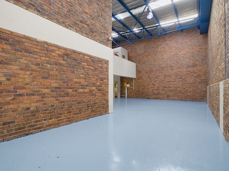 Spacious industrial utility area featuring high ceilings with exposed steel trusses, durable blue epoxy flooring, and classic face-brick walls.