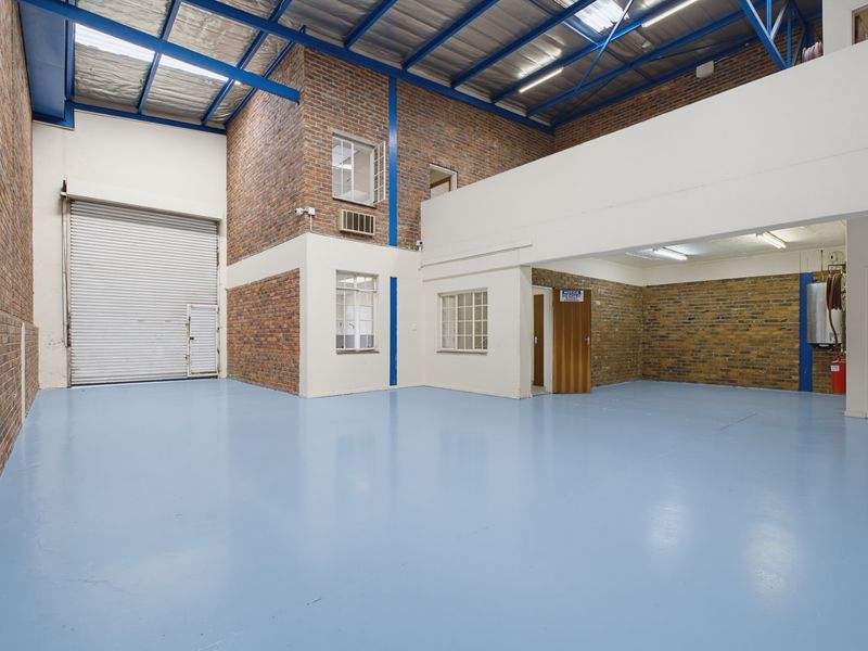 Spacious industrial warehouse unit featuring high ceilings with exposed steel trusses, durable epoxy flooring, roller shutter access, and a functional mezzanine level.