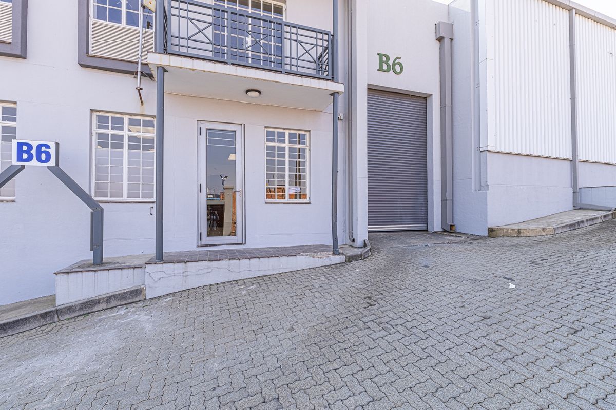 Industrial unit B6 featuring a roller shutter door, glass entrance, and a small balcony, situated on a paved driveway.