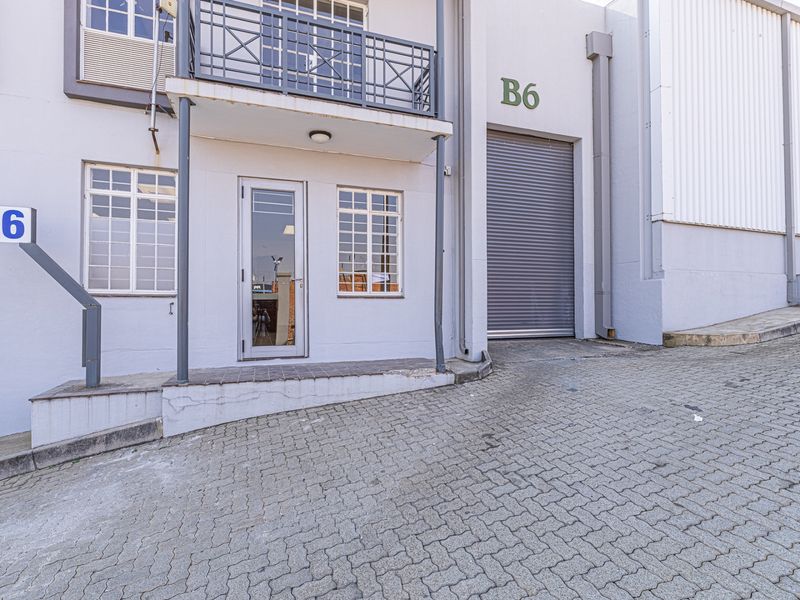 Industrial unit B6 featuring a roller shutter door, glass entrance, and a small balcony, situated on a paved driveway.