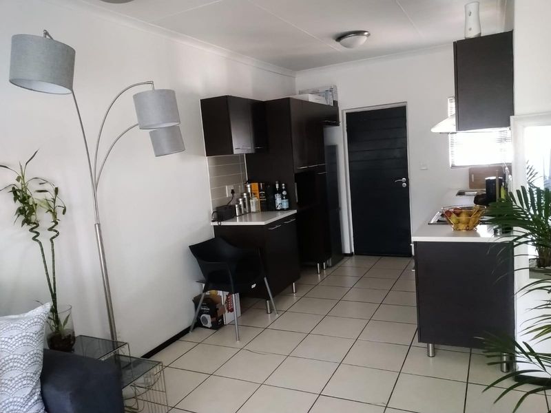 Open-plan kitchen area featuring dark cabinetry, tiled flooring, and integrated appliances, seamlessly connecting to the living space.