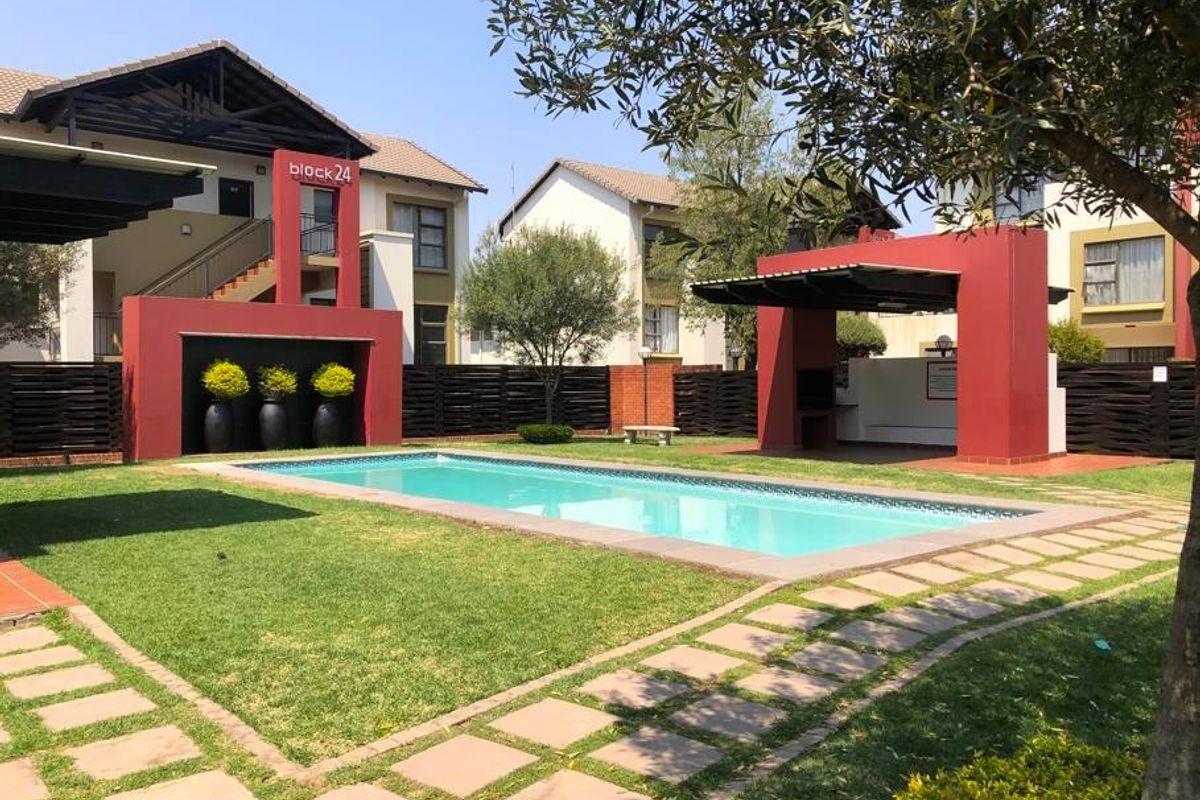 Communal pool area featuring a swimming pool, landscaped garden, and a covered braai area within a well-maintained apartment complex.