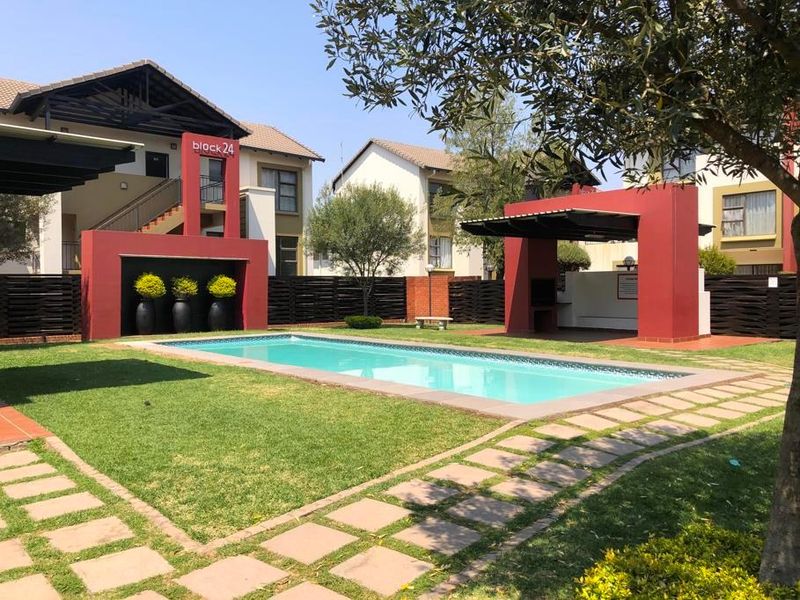 Communal pool area featuring a swimming pool, landscaped garden, and a covered braai area within a well-maintained apartment complex.