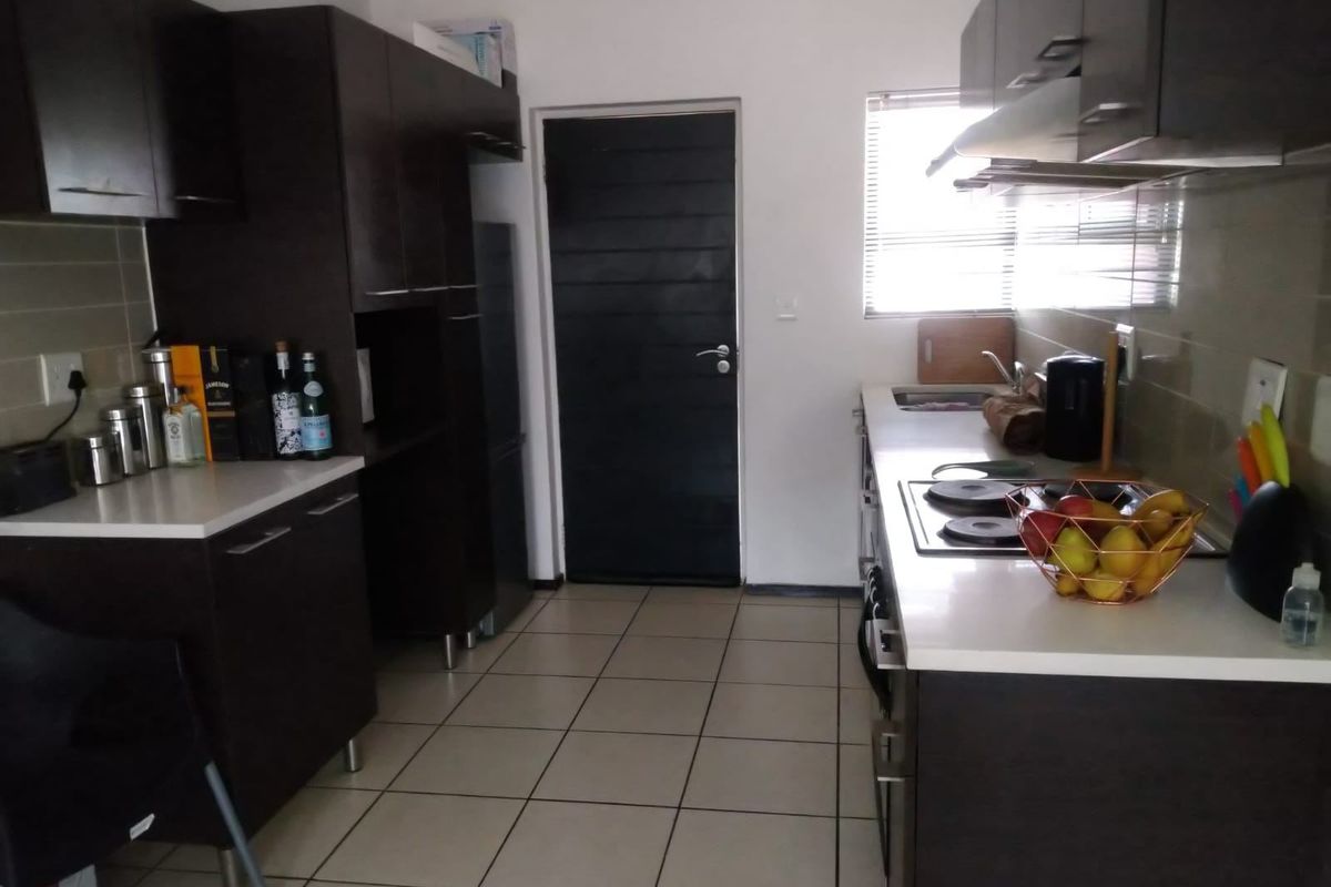 A functional kitchen featuring dark cabinetry, stone countertops, an integrated electric hob with extractor fan, and tiled flooring.