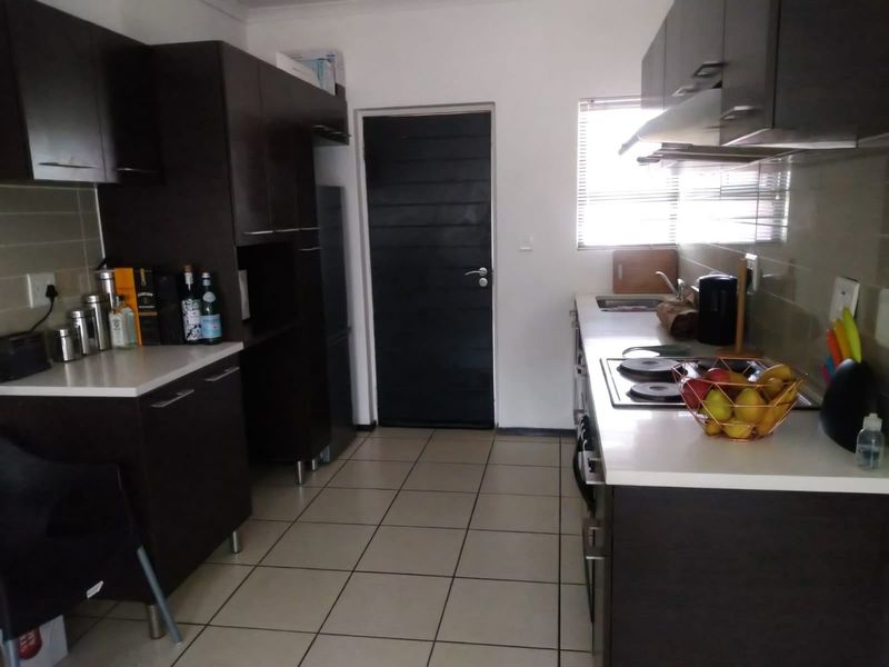 A functional kitchen featuring dark cabinetry, stone countertops, an integrated electric hob with extractor fan, and tiled flooring.