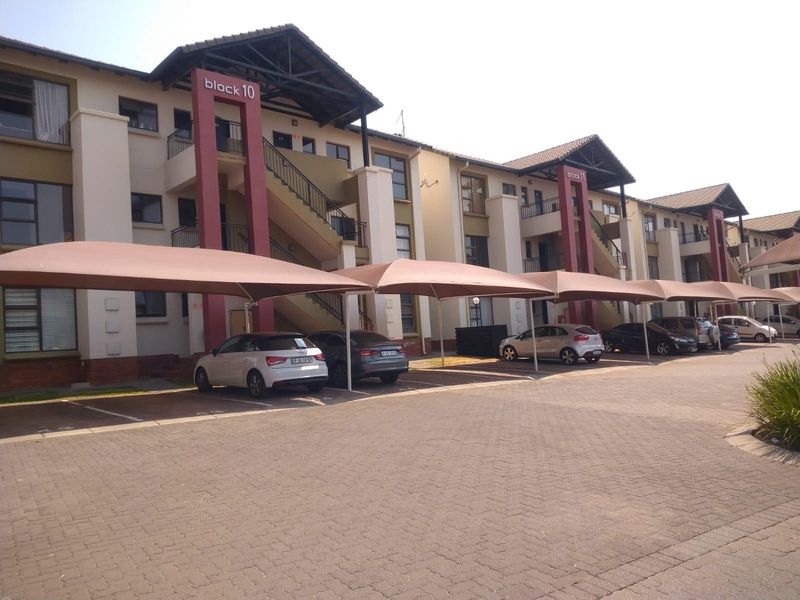 Exterior view of a multi-story apartment complex featuring paved parking areas with shade cloth carports and external staircases.