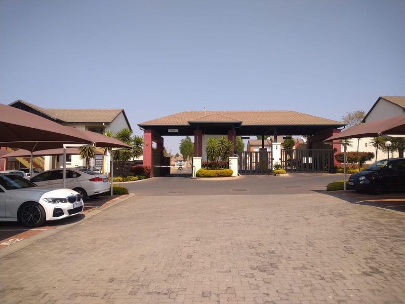 The entrance to the apartment complex features a secure gated access point, a guard house, and paved parking areas with shade cloth carports.