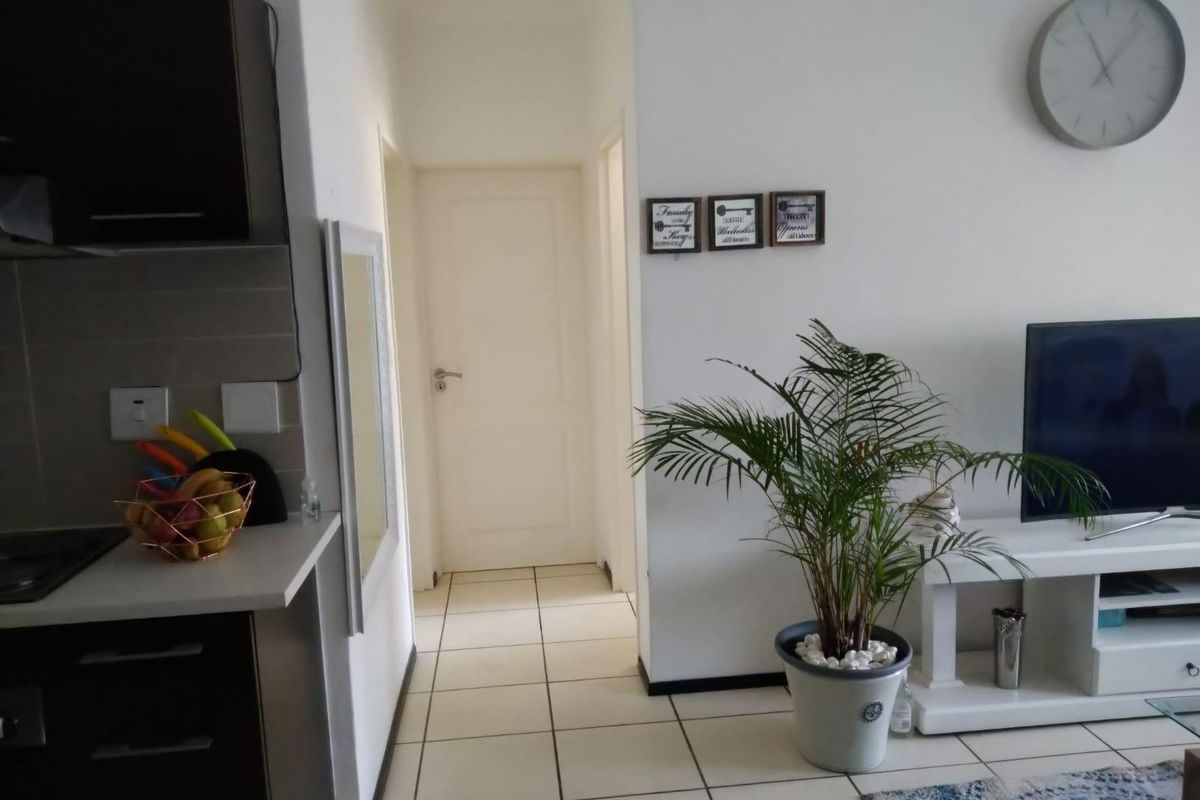Open plan living area featuring tiled flooring and a modern kitchen with built-in cabinetry, leading to a hallway with access to internal rooms.