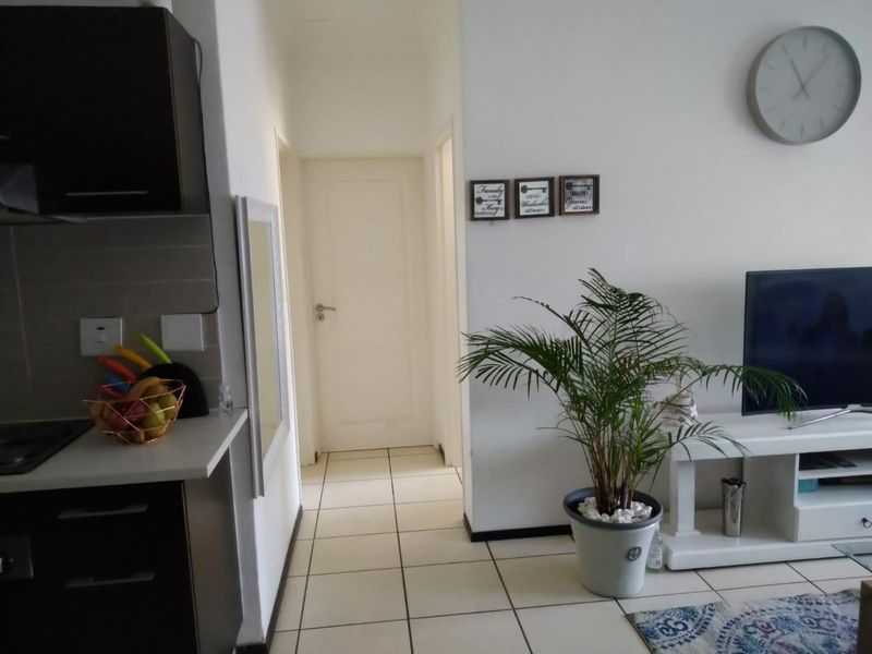Open plan living area featuring tiled flooring and a modern kitchen with built-in cabinetry, leading to a hallway with access to internal rooms.