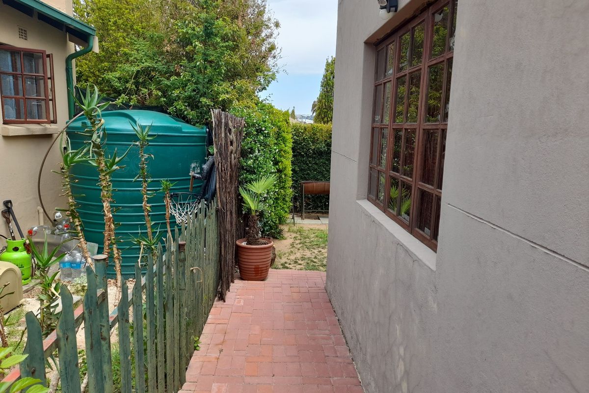 A side pathway featuring brick paving, a large water tank, and timber-framed windows along the exterior wall of the property.
