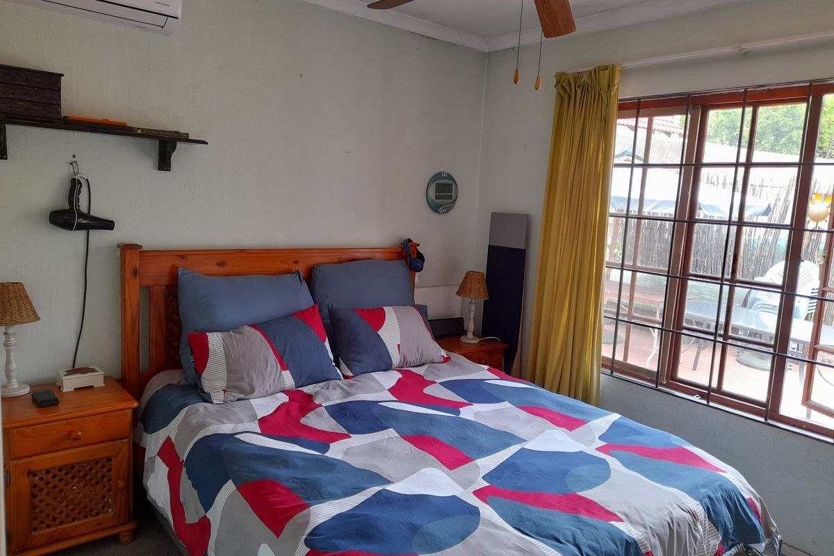 A functional bedroom featuring a ceiling fan, wall-mounted air conditioning unit, and large window with security bars.