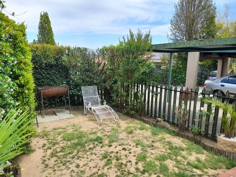 A small private garden area featuring a metal carport structure and perimeter fencing, with a dedicated paved area for outdoor cooking.