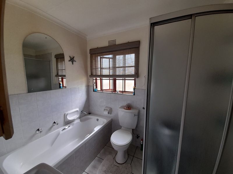 A functional bathroom featuring a built-in bathtub, separate shower enclosure, toilet, and tiled finishes, offering a clean and practical layout.
