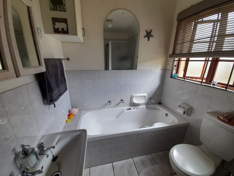 A functional bathroom featuring a built-in bathtub, pedestal basin, toilet, and tiled finishes, offering a practical layout with natural light from the window.
