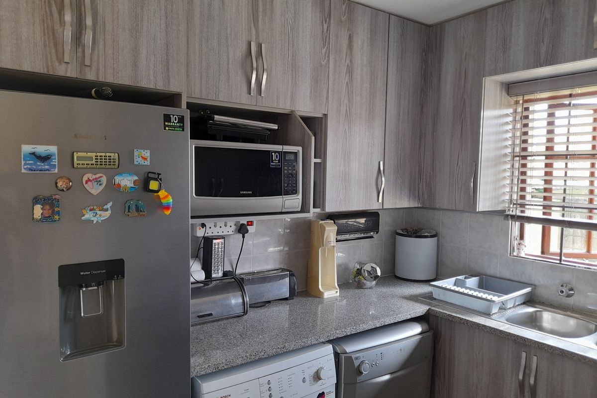 A functional kitchen featuring wood-grain cabinetry, granite countertops, a stainless steel sink, and integrated space for laundry appliances.