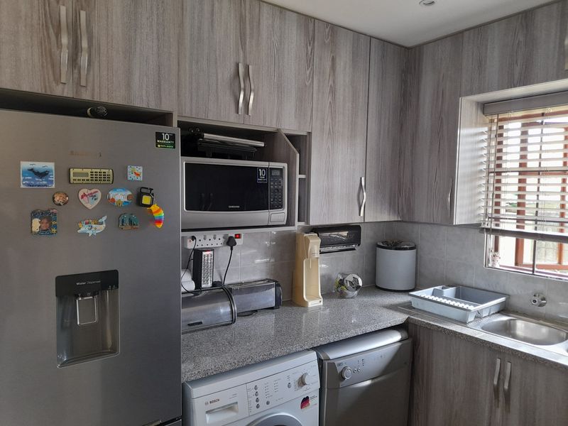 A functional kitchen featuring wood-grain cabinetry, granite countertops, a stainless steel sink, and integrated space for laundry appliances.