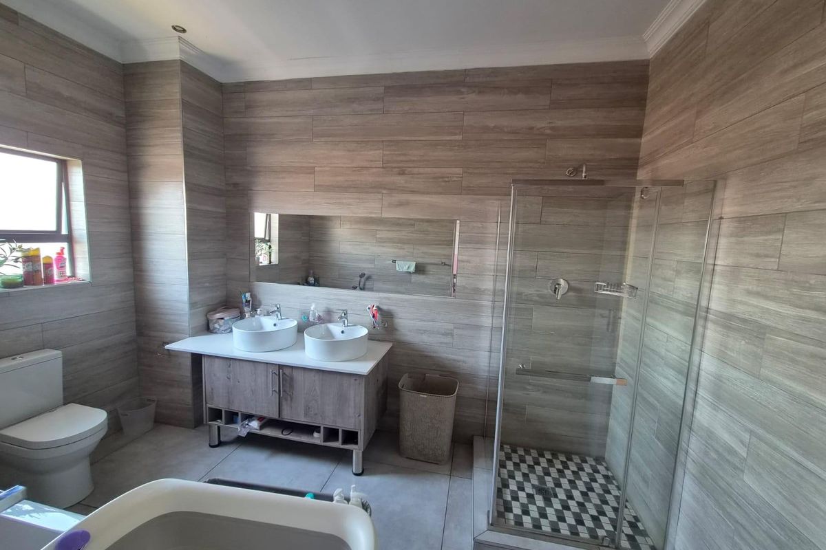 Modern bathroom featuring a double vanity with vessel sinks, a glass-enclosed shower with decorative floor tiling, and neutral wood-look wall tiles.