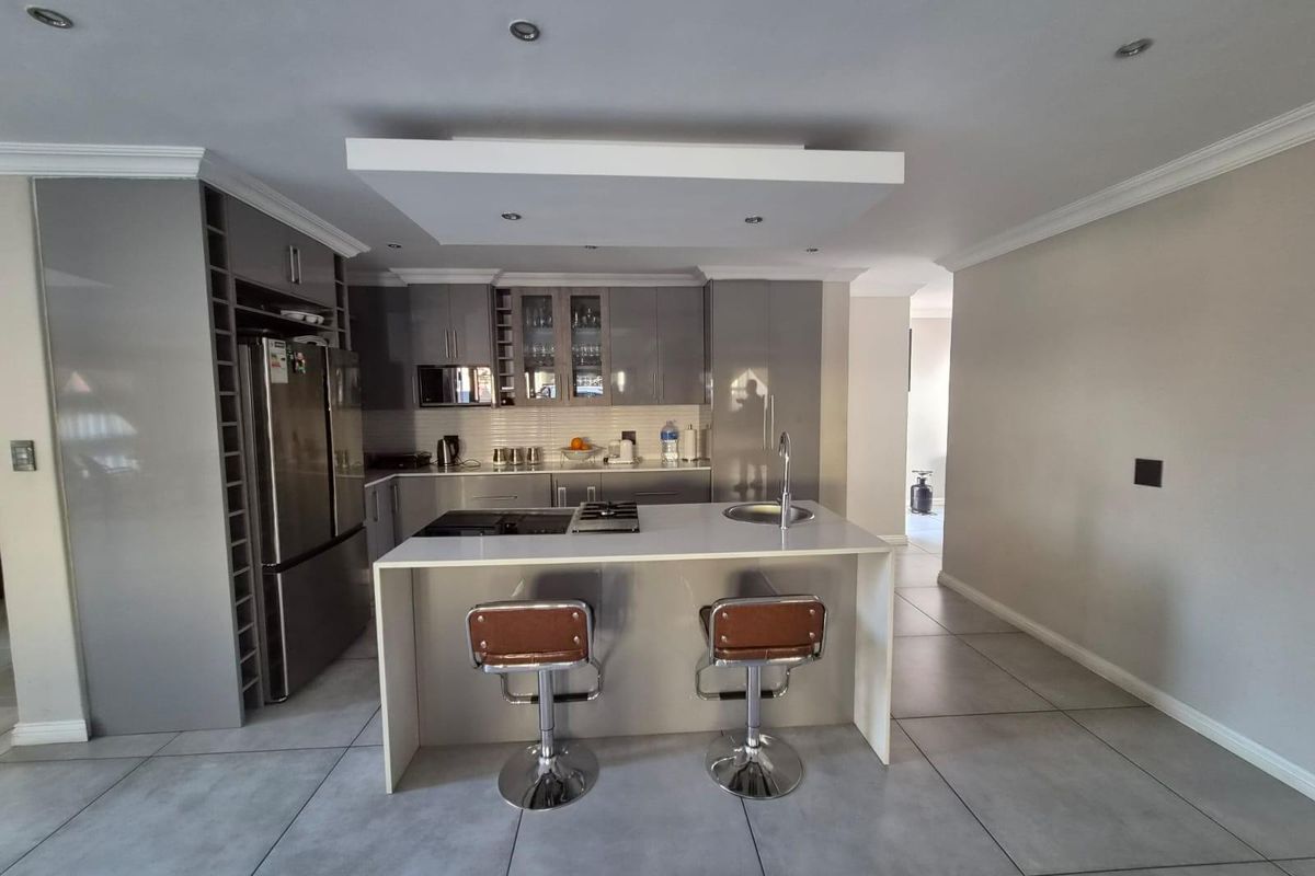 Modern kitchen featuring sleek grey cabinetry, a central island with a built-in hob, stone countertops, and large format floor tiles.
