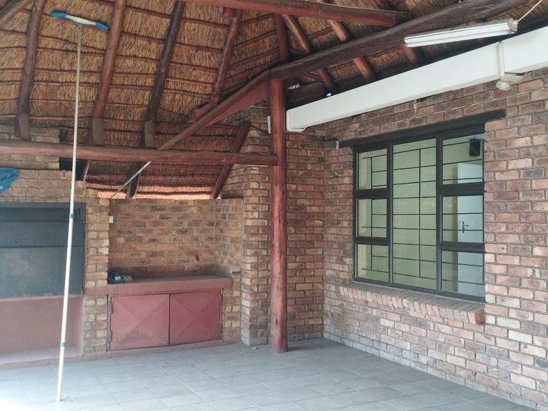 Covered outdoor patio area featuring a traditional thatched roof, exposed timber beams, and a built-in brick braai facility.