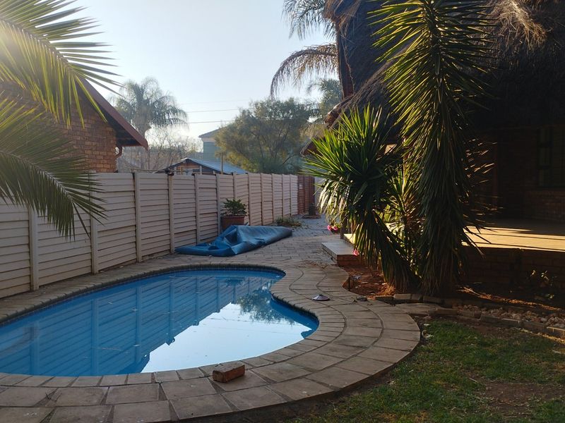 Outdoor pool area featuring a kidney-shaped swimming pool with paved surround, enclosed by a precast concrete boundary wall and adjacent to a thatched structure.