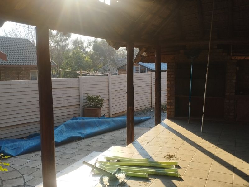 Covered outdoor patio featuring a thatched roof, timber support posts, tiled flooring, and a built-in brick braai area.