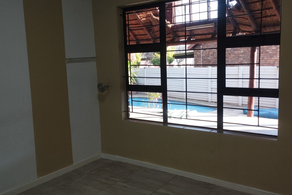 An empty bedroom featuring tiled flooring and security bars on the window, with a view overlooking the backyard pool area.