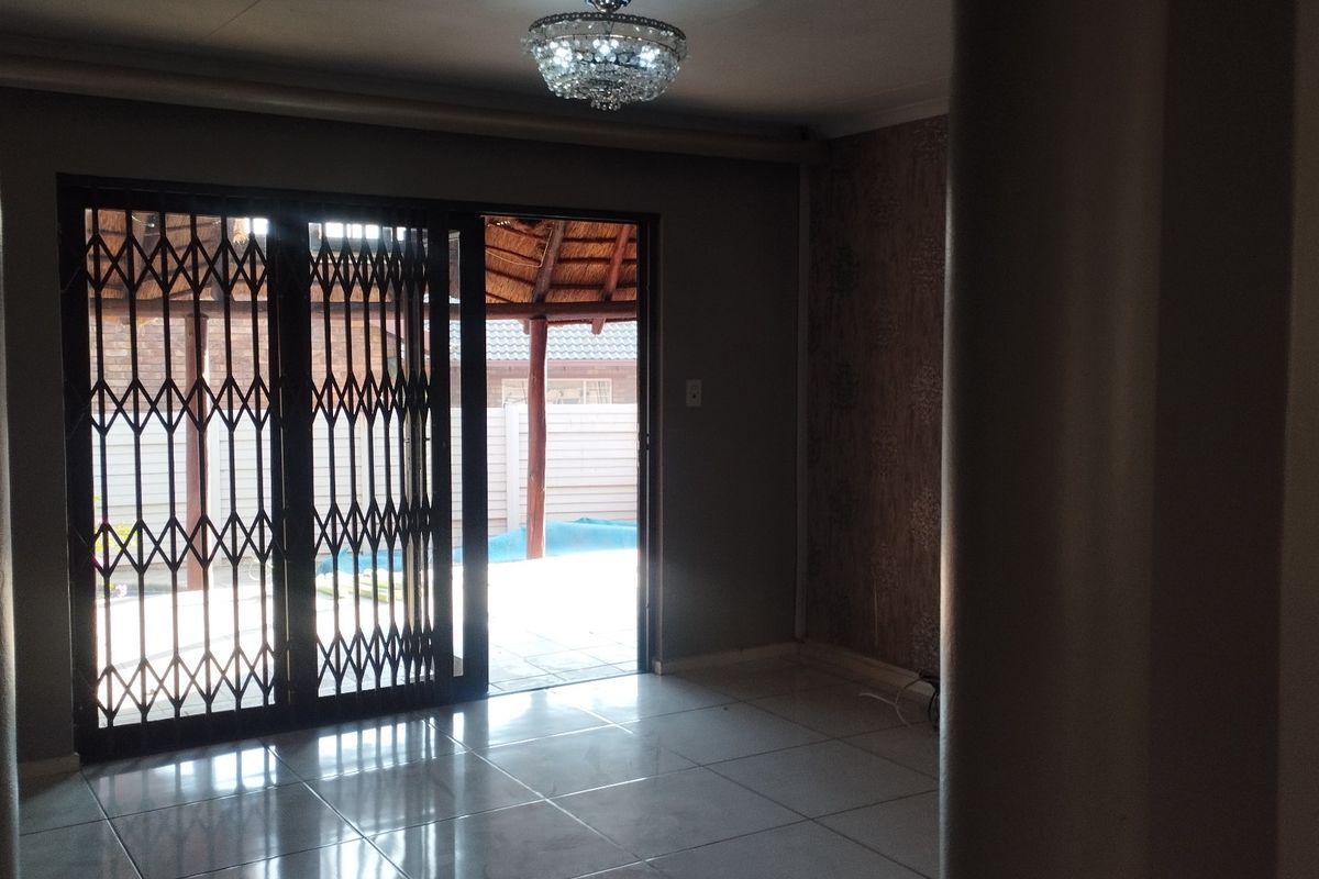 An empty living room featuring tiled flooring, a decorative crystal chandelier, and a sliding security gate leading to an outdoor patio area.