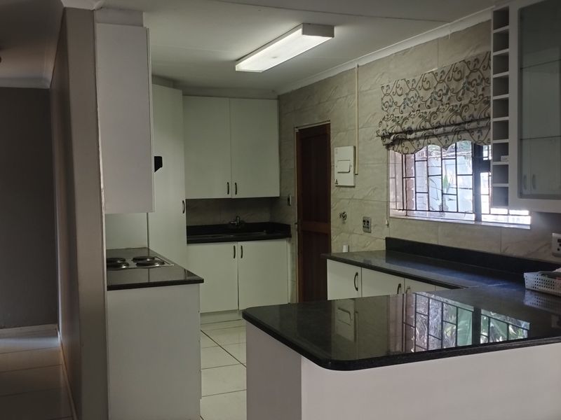 A functional kitchen featuring granite countertops, white cabinetry, an electric hob, and tiled flooring, offering a clean and practical workspace.